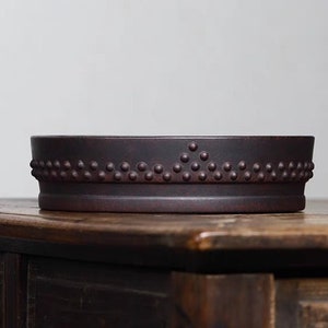 Könnte beinhalten: Ein dunkelbraunes Keramik-Teebrett mit einem strukturierten Rand. Der Rand hat ein sich wiederholendes Muster aus kleinen erhabenen Punkten.