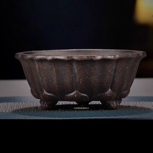 May include: A dark brown ceramic planter with a scalloped rim and three feet. The planter has a textured surface.