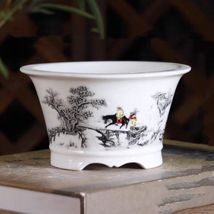 May include: White ceramic planter with a black and white landscape design featuring a horse and two figures. The planter has a rounded shape and a slightly flared rim.