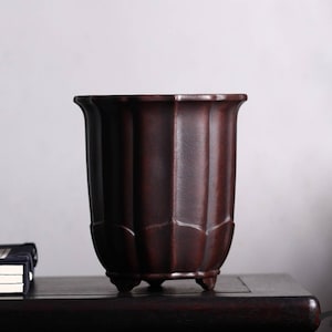 May include: A dark brown ceramic planter with a fluted design and four small feet. The planter is empty and has a smooth, matte finish.