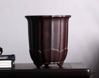 Puede incluir: Un macetero de cerámica marrón oscuro con un diseño acanalado y cuatro pequeños pies. El macetero está vacío y tiene un acabado liso y mate.