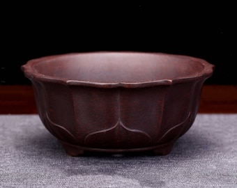 May include: A dark brown ceramic pot with a scalloped rim and a lotus flower design. The pot has three small feet and is ideal for displaying small plants.