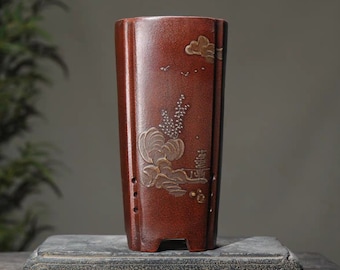 May include: A terracotta-colored ceramic planter with a rectangular shape and a decorative design of a mountain scene with clouds and birds. The planter has drainage holes and a slightly flared rim.