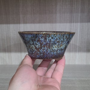 May include: A blue and brown ceramic planter with a speckled glaze. The planter has a wide, shallow bowl shape and three small feet.