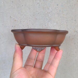 以下が含まれることがあります： 3本の脚が付いた、茶色の八角形の盆栽鉢。鉢は陶器製で、マットな仕上がりです。