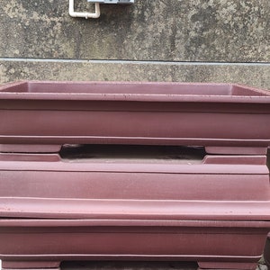 May include: Three stacked terracotta plant pots in a deep reddish-brown color. The pots are rectangular with rounded edges and have a slightly textured surface.