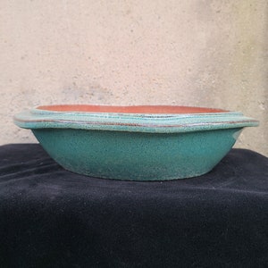 Peut inclure: Un pot à bonsaï en céramique émaillée turquoise, de forme arrondie avec un bord légèrement surélevé. Le pot a un intérieur en terre cuite brun clair.
