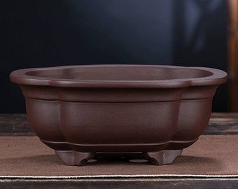 May include: A brown ceramic planter with a rounded oval shape and a slightly flared rim. The planter has four short legs and a smooth, matte finish.