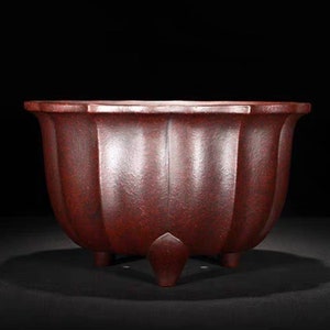 May include: A dark red, ceramic planter with a fluted design and three legs. The planter is made in a traditional style.
