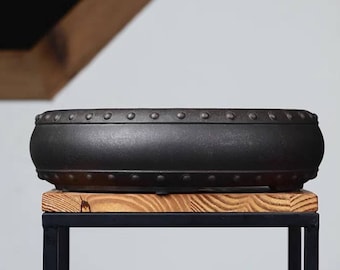 May include: A black ceramic bonsai pot with a rounded shape and a decorative rim of metal studs. The pot is sitting on a wooden stand.