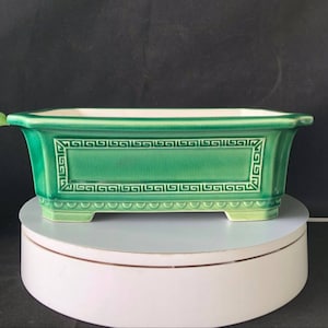 Puede incluir: Un macetero rectangular de cerámica verde con interior blanco y un diseño geométrico alrededor del borde. El macetero tiene cuatro pequeñas patas.