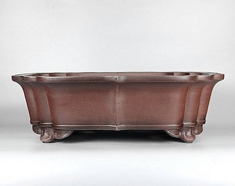 May include: A large, dark brown, unglazed ceramic bonsai pot with a scalloped rim and three feet. The pot is rectangular with rounded corners.