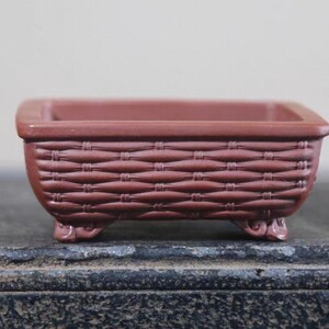 Peut inclure: Petit pot de fleurs rectangulaire en c&eacute;ramique brun rouge&acirc;tre avec un motif de panier tress&eacute;. Le pot a un dessus carr&eacute; et repose sur quatre petits pieds d&eacute;coratifs. Id&eacute;al pour les petites plantes ou les succulentes.