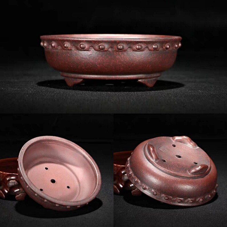 May include: A terracotta bonsai pot with a rounded shape and a textured rim. The pot has three small feet and a drainage hole in the bottom.