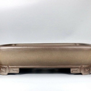 May include: A rectangular brown bonsai pot with a textured surface and a decorative design around the rim and base.