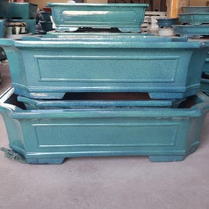 May include: Two stacked blue ceramic rectangular planters with decorative edges. The planters are empty and ready for planting.