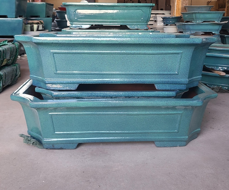 May include: Two stacked blue ceramic rectangular planters with decorative edges. The planters are empty and ready for planting.