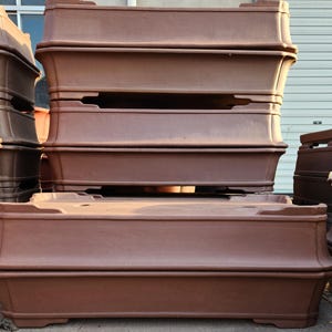 May include: A stack of four brown rectangular planter boxes made of plastic. The boxes are stacked on top of each other, with the largest box at the bottom and the smallest box at the top.