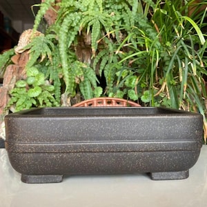 Puede incluir: Una taza de cerámica blanca con un asa negra y el texto "But First, Coffee" en negrita negra. La taza se encuentra sobre un fondo borroso, resaltando su diseño limpio.