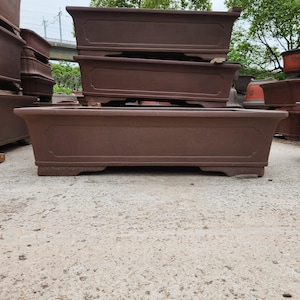 May include: A stack of rectangular, brown ceramic planters. The planters have a simple, classic design with a slightly raised border and are suitable for outdoor use. The planters are of varying sizes and are stacked on top of each other.