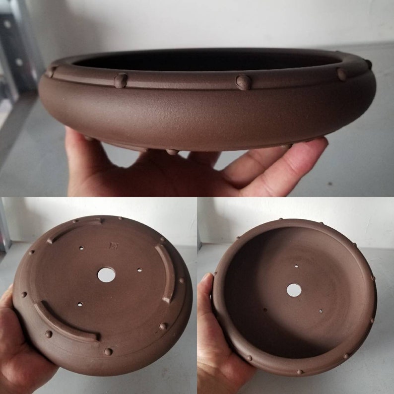 K&ouml;nnte beinhalten: Ein brauner Keramik-Bonsai-Topf mit runder Form und einem erh&ouml;hten Rand. Der Topf hat ein kleines Abzugsloch im Boden und eine Reihe kleiner Noppen am Rand.