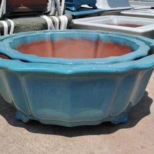 Puede incluir: Un macetero grande de cerámica azul con un borde festoneado. El macetero está hecho de dos piezas, una encajada dentro de la otra. El macetero está vacío y listo para ser llenado con plantas.
