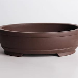 May include: A brown oval ceramic planter with three short legs. The planter is made of unglazed terracotta and has a slightly textured surface.
