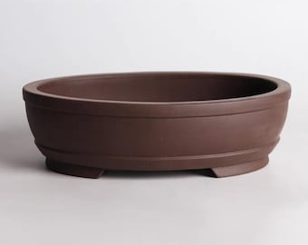 Puede incluir: Un macetero ovalado de cerámica marrón con tres patas cortas. El macetero está hecho de terracota sin esmaltar y tiene una superficie ligeramente texturizada.
