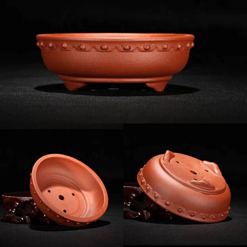 May include: A terracotta bonsai pot with a rounded shape and a decorative rim. The pot has three small feet and drainage holes in the bottom.