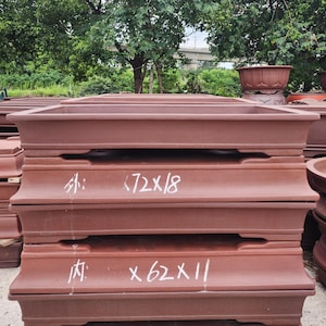 May include: A stack of rectangular terracotta bonsai pots with a matte finish. The top pot features white painted text reading 72x18, and the bottom pot features white painted text reading 62x11, indicating dimensions in centimetres.
