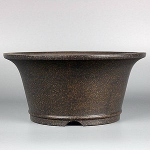 May include: A dark brown ceramic bonsai pot with a wide, rounded base and a flared rim. The pot has a textured surface and a slightly raised lip around the rim.