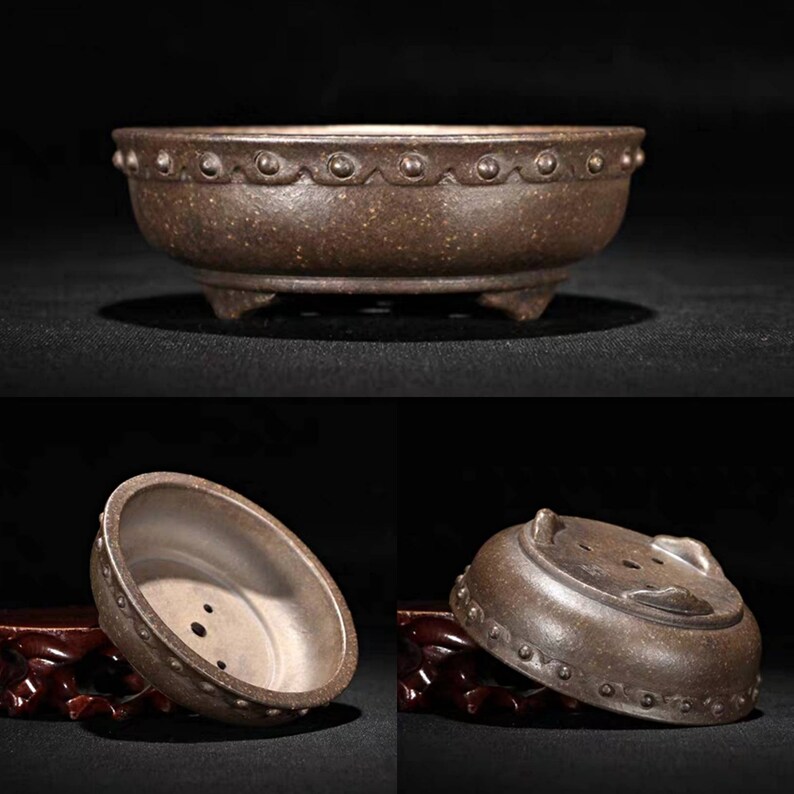 May include: A brown ceramic bonsai pot with a rounded shape and a decorative rim. The pot has three small feet and drainage holes in the bottom.