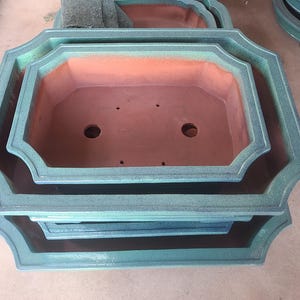 May include: A set of three green ceramic planter pots with a scalloped rim. The pots are nested inside each other, with the largest pot at the bottom and the smallest pot at the top.