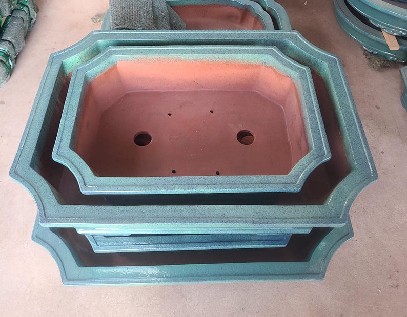 May include: A set of three green ceramic planter pots with a scalloped rim. The pots are nested inside each other, with the largest pot at the bottom and the smallest pot at the top.