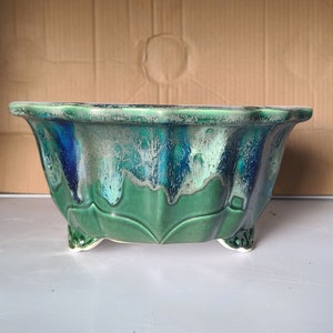 Può includere: Un vaso in ceramica verde e blu con un bordo a festoni e tre gambe. Il vaso ha una smaltatura screziata con un motivo bianco e blu.