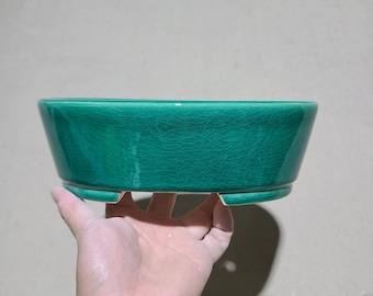 May include: A green ceramic bonsai pot with a crackled glaze and a rounded oval shape. The pot has three small feet on the bottom.