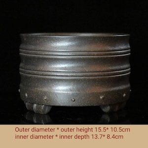 May include: A dark brown ceramic planter with a rounded shape and three feet. The planter has a textured surface and a series of raised rings around the sides. The planter measures 15.5 inches in diameter and 10.5 inches in height. The inner diameter is 13.7 inches and the inner depth is 8.4 inches.