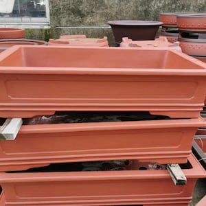 May include: Three terracotta bonsai pots stacked on top of each other. The pots are rectangular with a raised lip around the top edge and a decorative lip around the bottom edge.