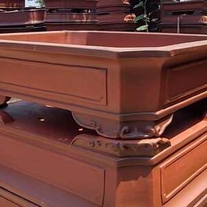 Pode incluir: Uma pilha de vasos de bonsai retangulares grandes, cor de terracota. Cada vaso tem um painel decorativo na frente e &eacute; suportado por p&eacute;s ornamentados. Os vasos s&atilde;o projetados para uso externo e s&atilde;o empilhados para armazenamento.