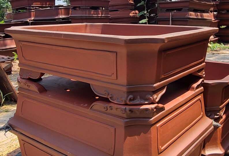 Pode incluir: Uma pilha de vasos de bonsai retangulares grandes, cor de terracota. Cada vaso tem um painel decorativo na frente e &eacute; suportado por p&eacute;s ornamentados. Os vasos s&atilde;o projetados para uso externo e s&atilde;o empilhados para armazenamento.