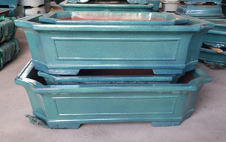 May include: Two stacked rectangular ceramic bonsai pots with a teal glaze. The pots have a raised rim and a decorative design around the top edge.