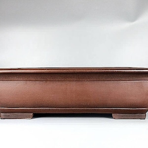 May include: A rectangular brown bonsai pot with a slightly rounded bottom and four small feet. The pot is made of a textured ceramic material.