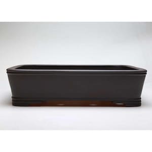 Puede incluir: Una maceta rectangular de color marrón oscuro para bonsái, con un borde ligeramente curvado y líneas horizontales decorativas cerca de la base. La maceta está diseñada con un perfil bajo y una estética simple y elegante, adecuada para bonsáis.