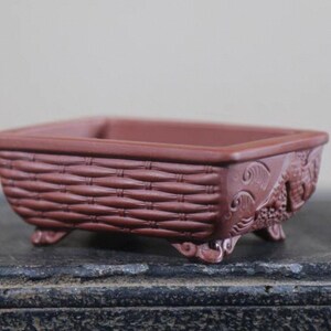 Peut inclure: Un pot &agrave; bonsa&iuml; rectangulaire brun rouge&acirc;tre avec un motif de panier tress&eacute; sur les c&ocirc;t&eacute;s. Le pot comporte des sculptures d&eacute;coratives sur les coins et repose sur de petits pieds. Le pot est con&ccedil;u pour la culture de petites plantes.