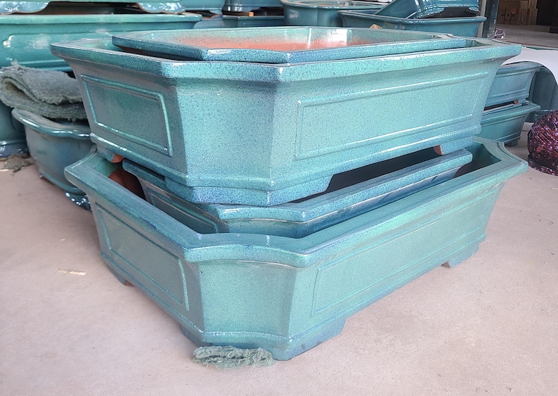 May include: Three stacked rectangular ceramic planters in a teal green color. The planters are made of glazed ceramic and have a textured surface.