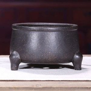 Op de afbeelding: Een zwarte keramische wierookbrander met drie poten. De brander heeft een ruw, getextureerd oppervlak.