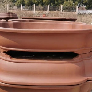Puede incluir: Dos macetas de terracota apiladas una encima de la otra. Las macetas son de forma ovalada con un borde ancho y una base elevada. Las macetas son de color marrón rojizo.