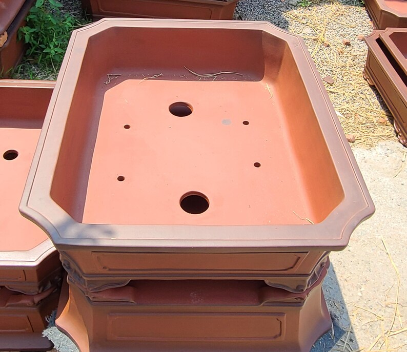 Pode incluir: Um grande vaso de bonsai de cor terracota com formato retangular e base decorativa em camadas. O vaso possui v&aacute;rios orif&iacute;cios de drenagem e uma bacia larga e rasa, adequada para plantar pequenas &aacute;rvores ou arbustos.