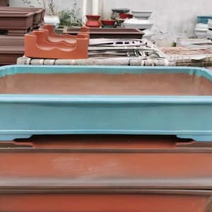 May include: A stack of three rectangular ceramic planters. The top planter is light blue and the bottom two are brown.