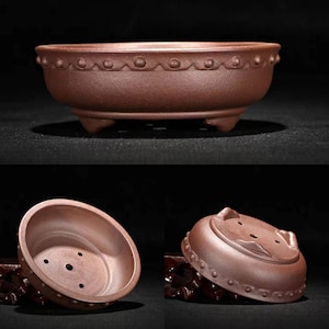 May include: A terracotta bonsai pot with a rounded shape and three legs. The pot has a decorative rim with small dots and a textured surface.